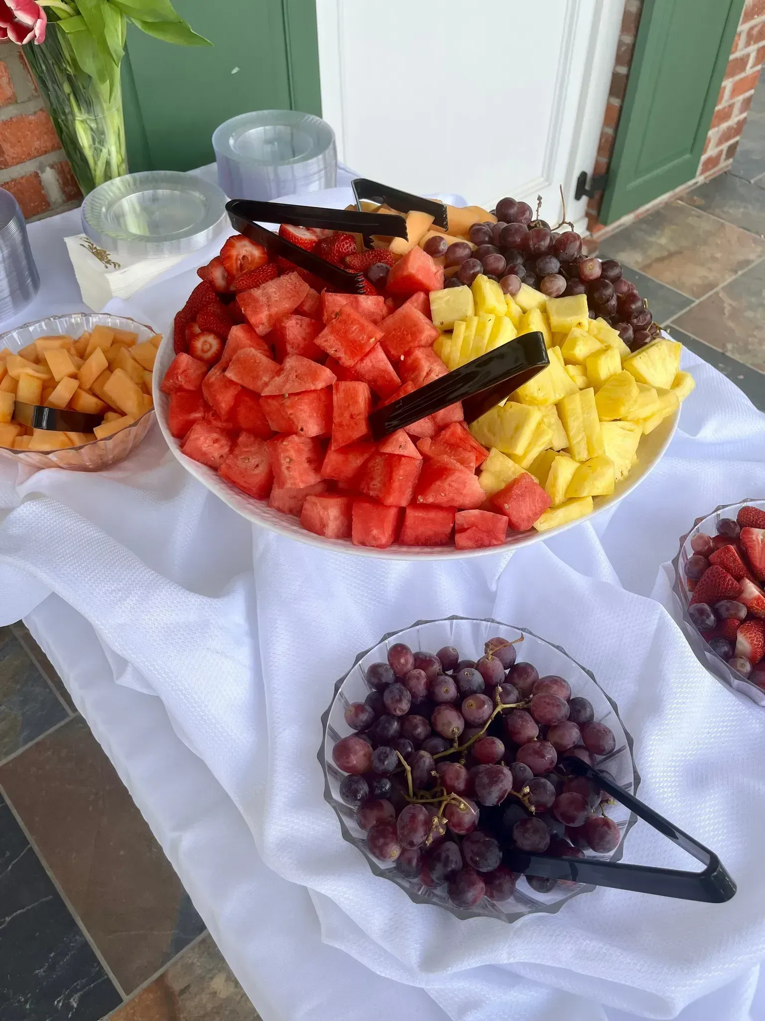 Fruit buffet with watermelon, pineapple, grapes, and bananas on a white-covered table