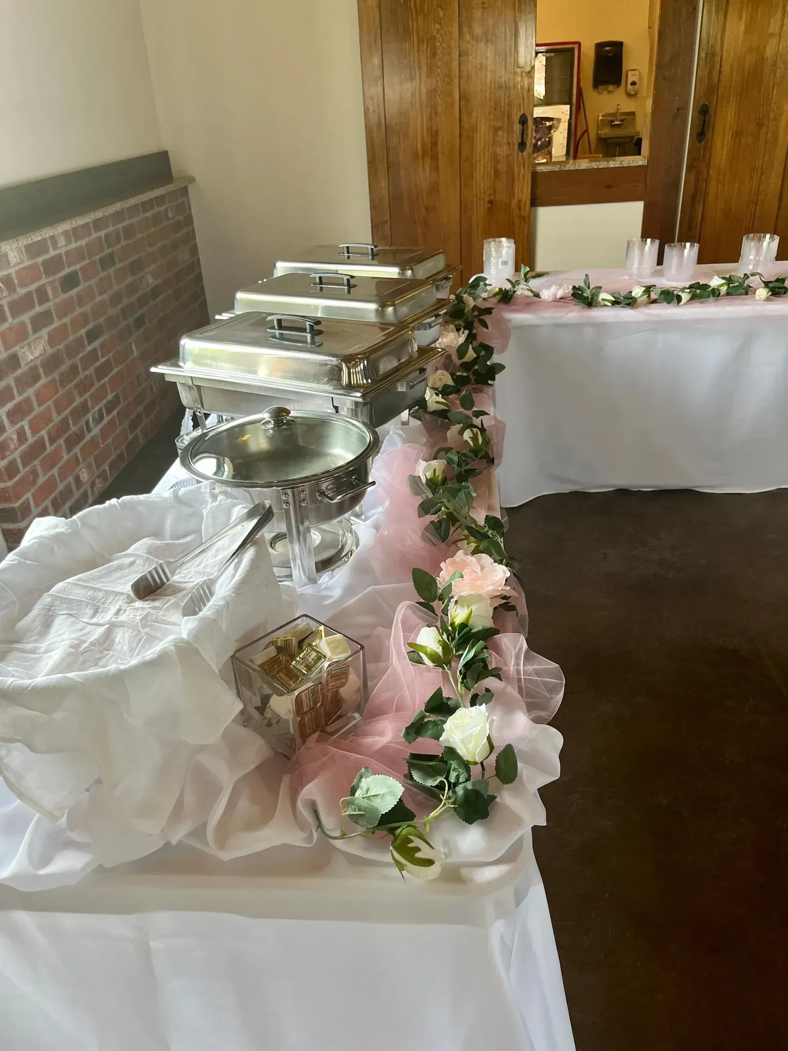 Buffet table with silver chafing dishes, white cloth, and pink floral garland in a banquet room