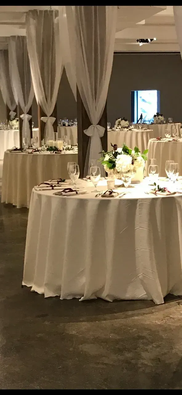 Elegant banquet hall with round draped tables, white chairs, and tall white fabric decor
