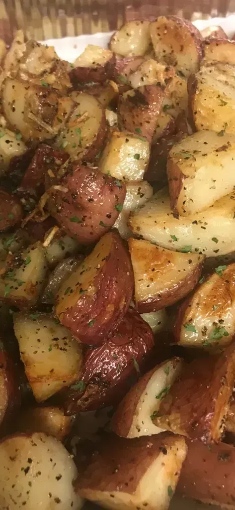 Roasted potato wedges with herb seasoning, browned edges, and glossy oil.