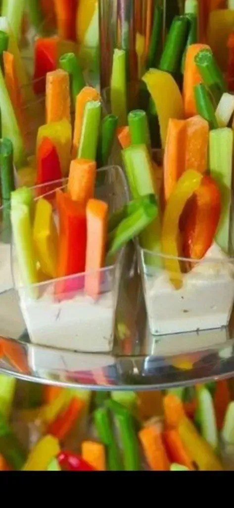 Colorful vegetable sticks in clear glasses, with carrots, cucumbers, and celery arranged vertically.