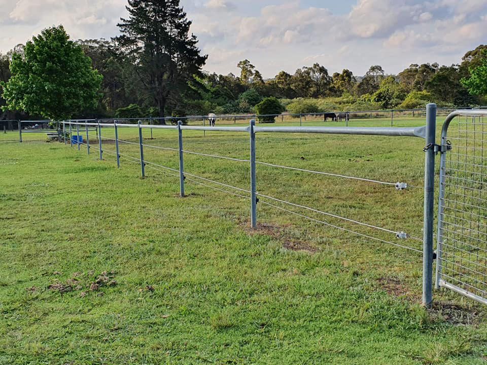 A Fence Surrounds A Grassy Field — McCarthys Property Services in Woolgoolga, NSW
