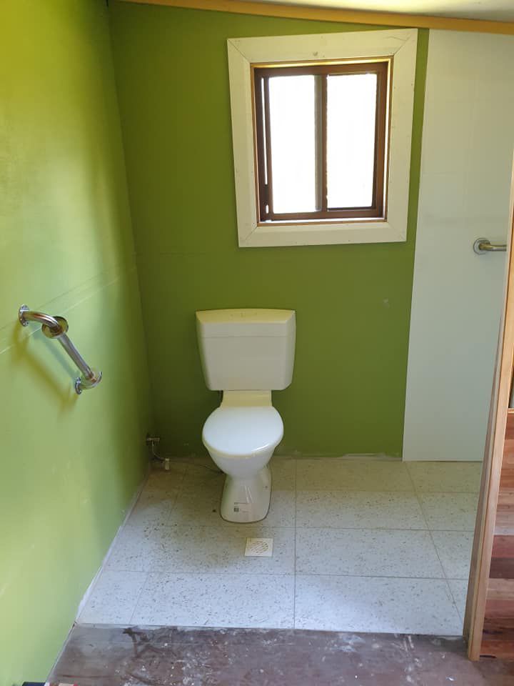 A Bathroom With A Toilet , Window And Green Walls — McCarthys Property Services in Glenugie, NSW