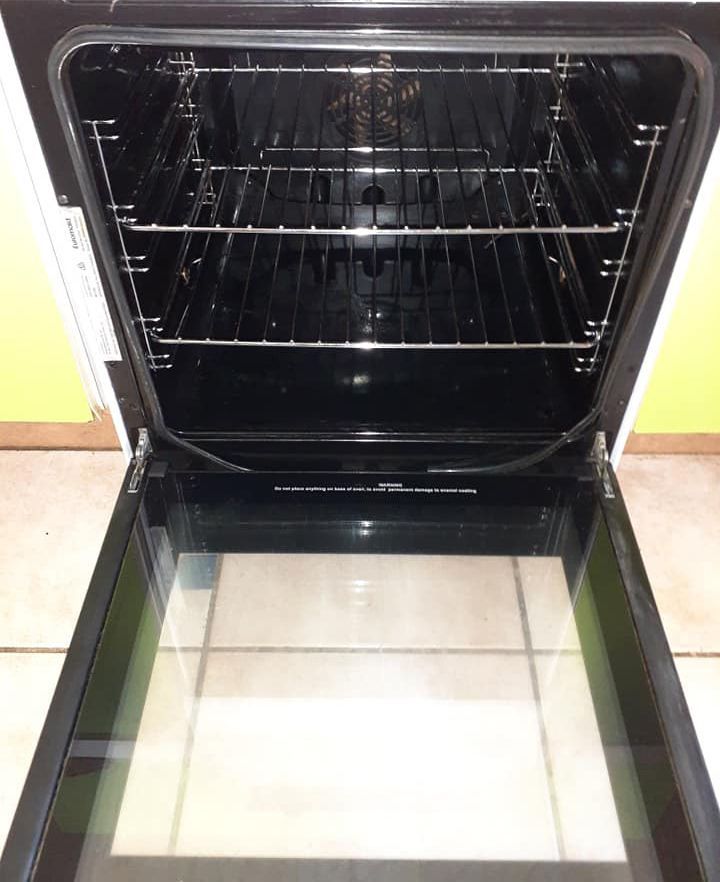 An Empty Oven With The Door Open Is Sitting On A Tiled Floor After Cleaning — McCarthys Property Services in Glenugie, NSW