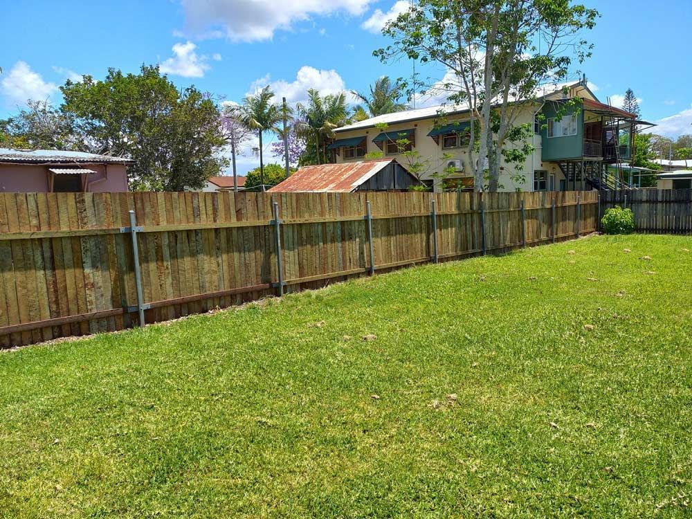 A Wooden Fence Surrounds A Lush Green Lawn In Front Of A House — McCarthys Property Services in Glenugie, NSW