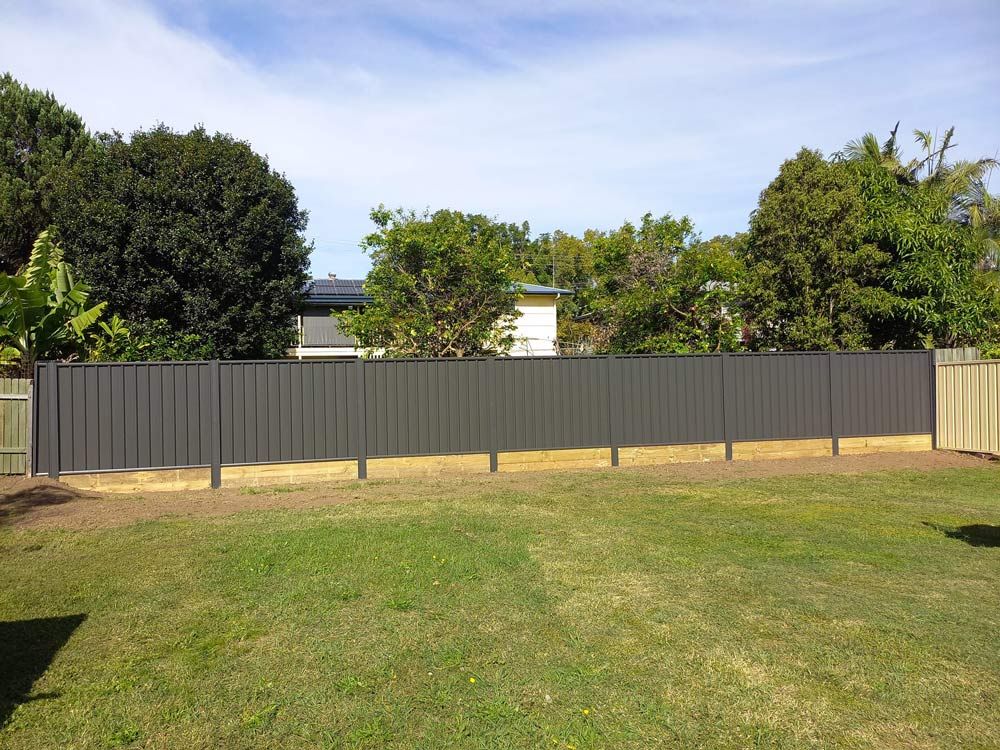 A Fence Surrounds A Lush Green Yard With Trees In The Background — McCarthys Property Services in Glenugie, NSW