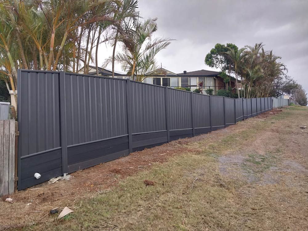 A Long Black Fence Surrounds A Grassy Field In Front Of A House — McCarthys Property Services in Yamba, NSW