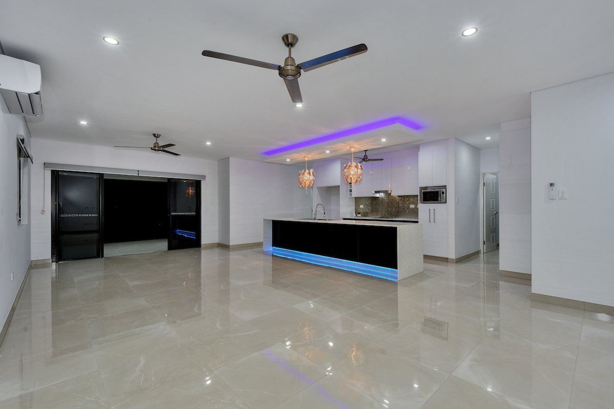 A living room with a ceiling fan and a kitchen in the background