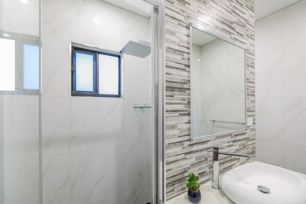 A bathroom with a sink , mirror , shower and window.