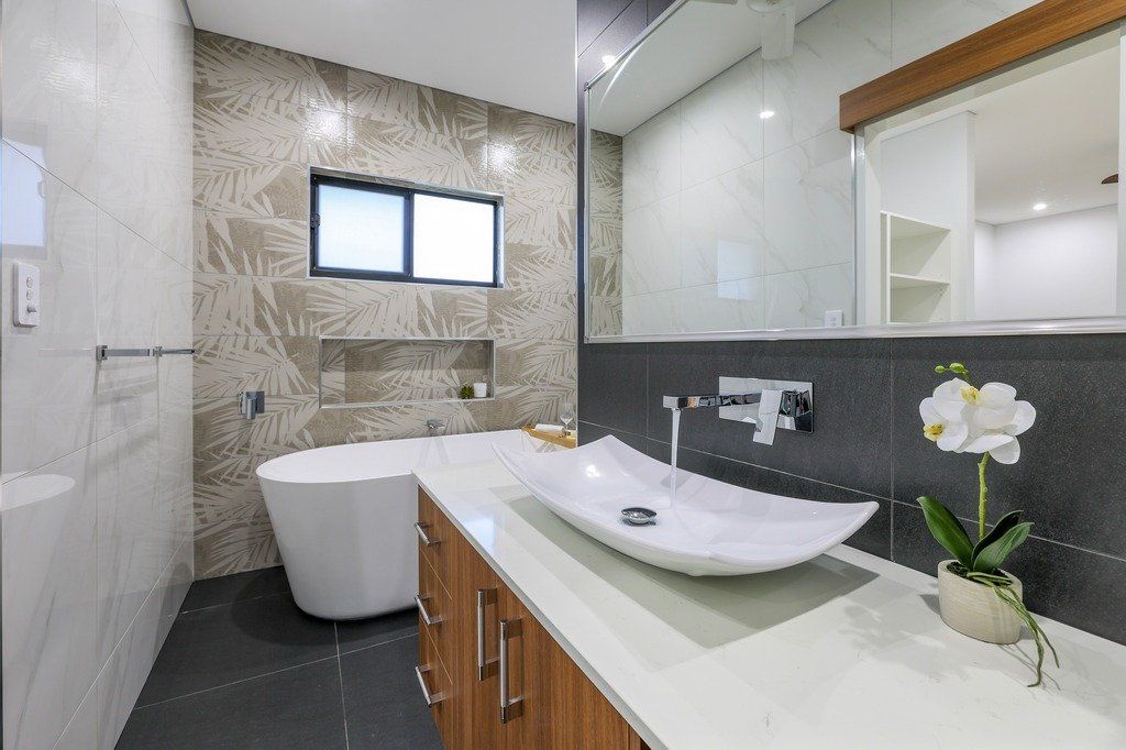 A bathroom with a sink , tub , mirror and orchids.