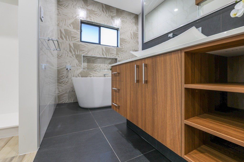A bathroom with a bathtub , sink , mirror and wooden cabinets.