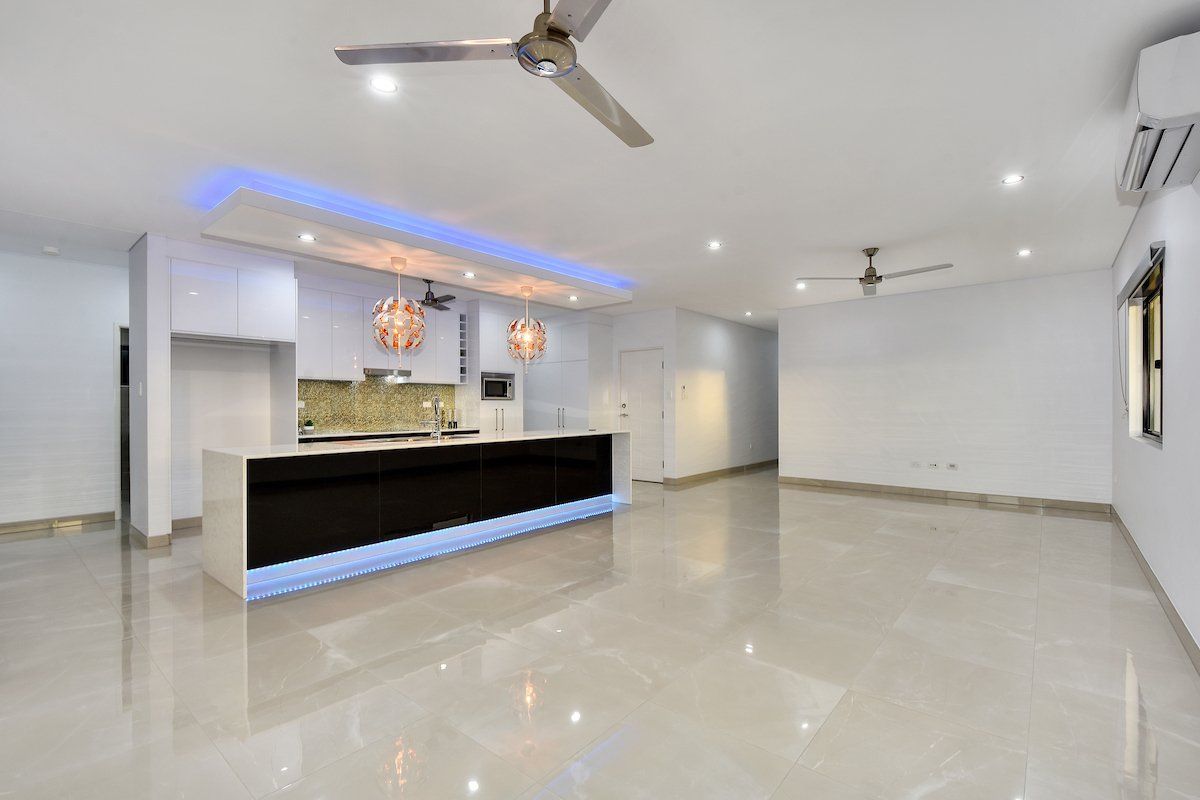 A large empty room with a kitchen and a ceiling fan.