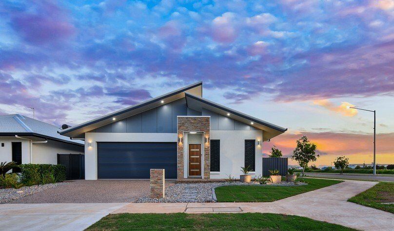 A modern house with a large garage and a sunset in the background.