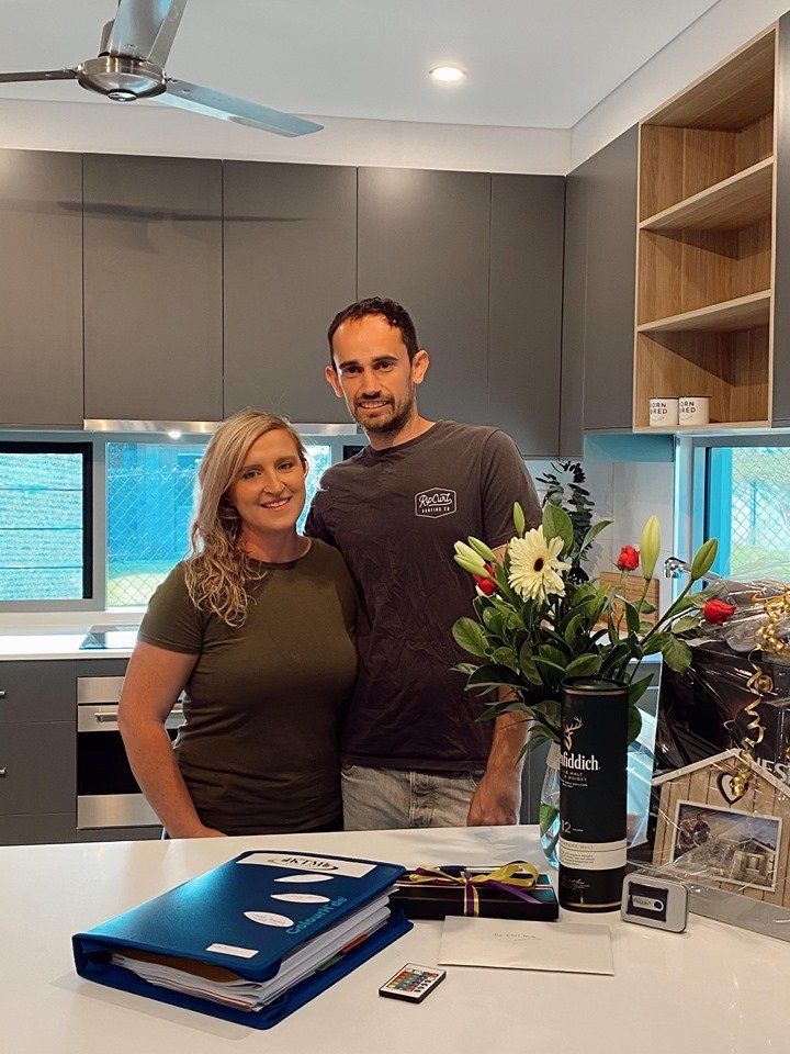 A man and a woman are standing in a kitchen next to a vase of flowers.
