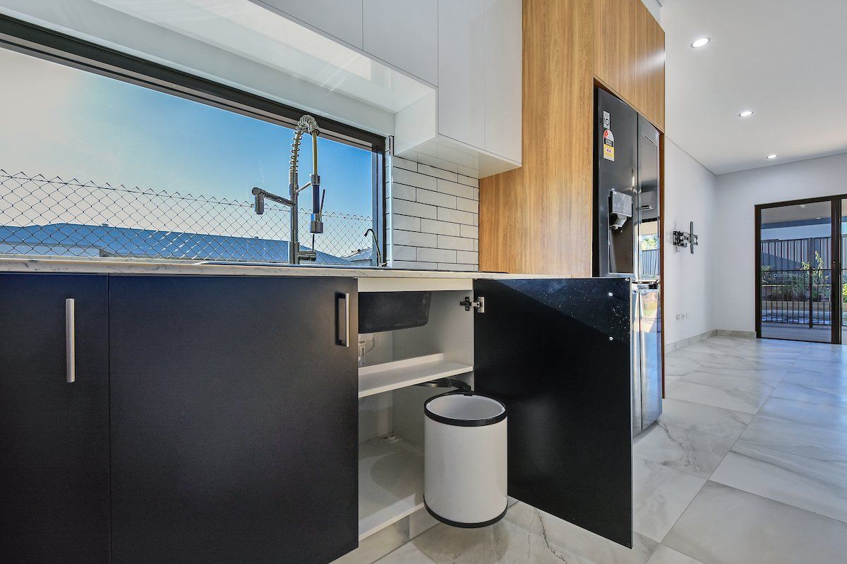 A kitchen with black cabinets and a white trash can.