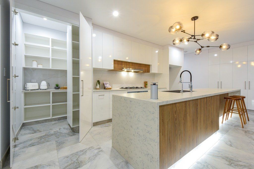 A kitchen with white cabinets , a large island , and a pantry.