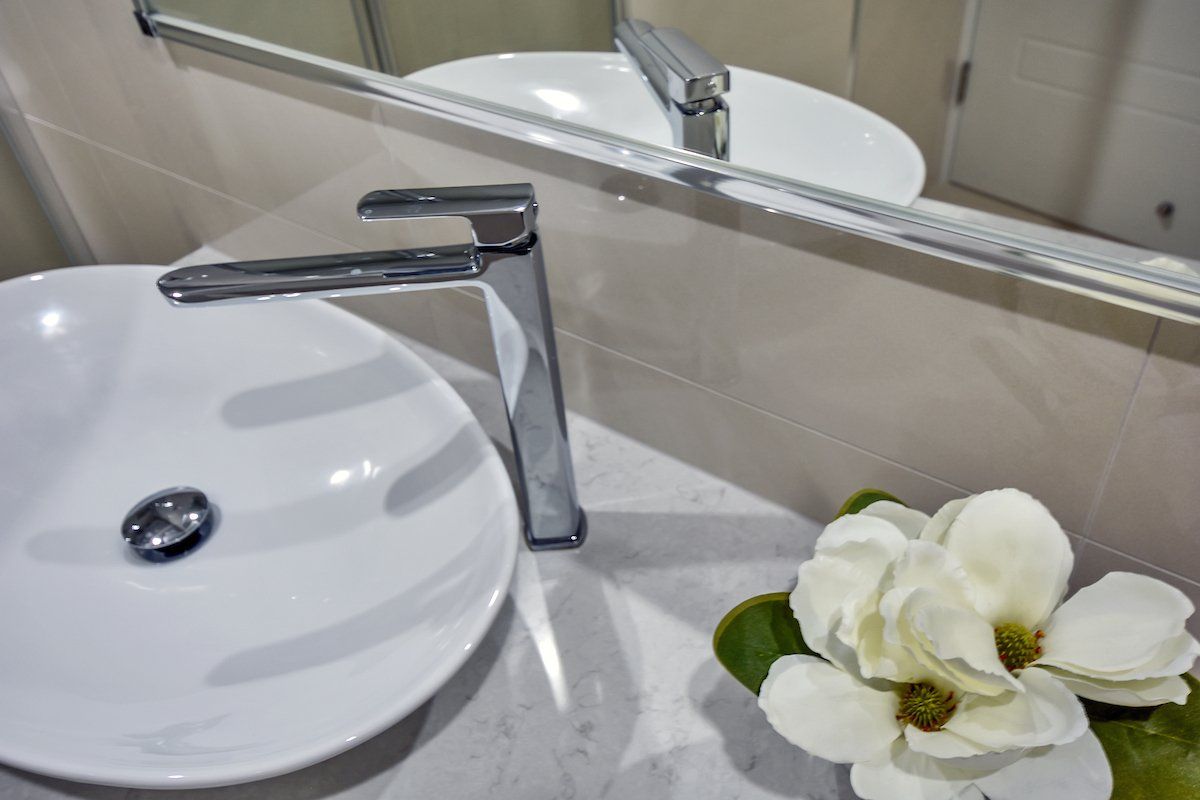 A bathroom sink with a flower in front of it and a mirror.