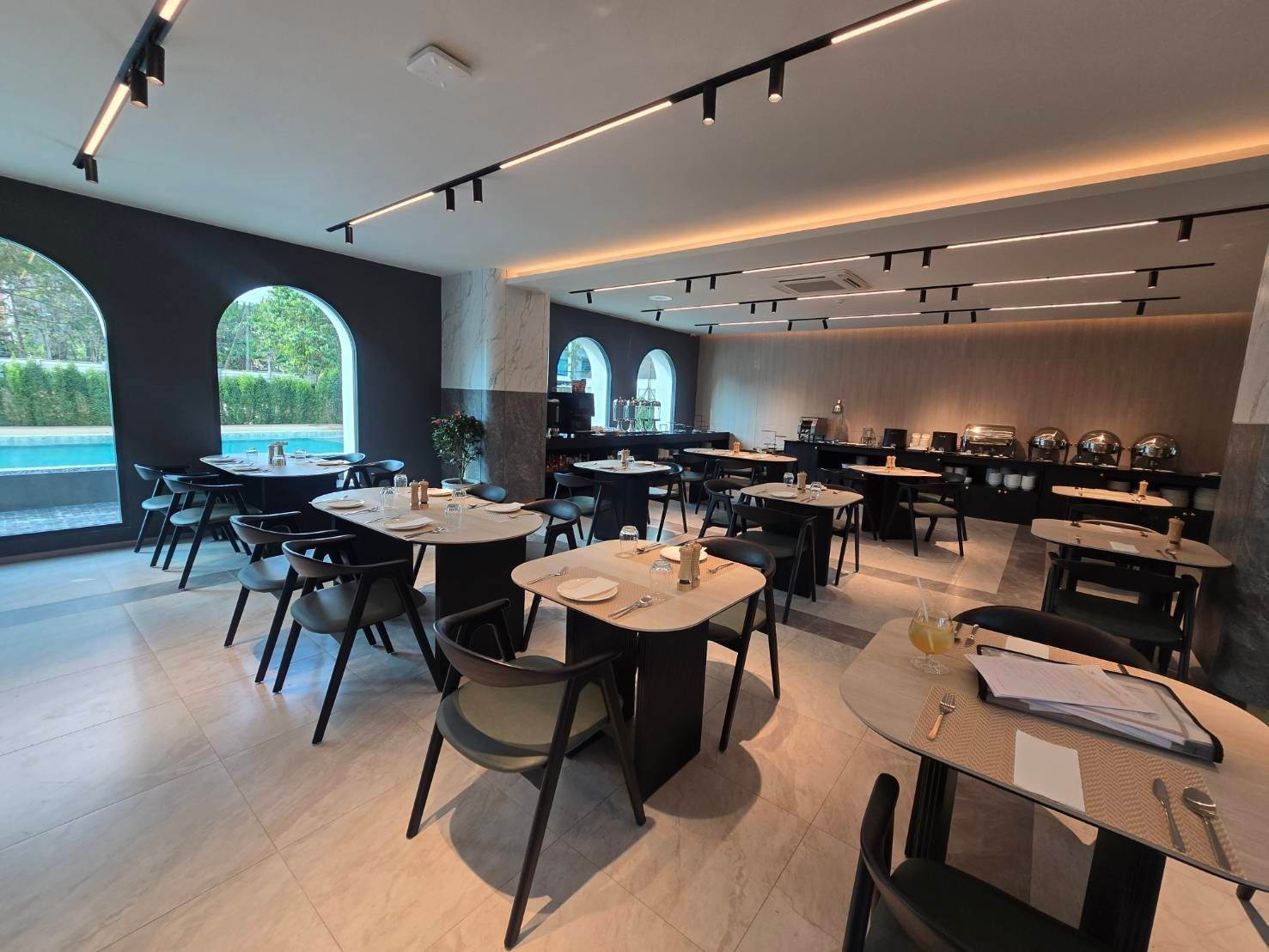 Modern empty restaurant dining room with round tables, black chairs, and large arched windows