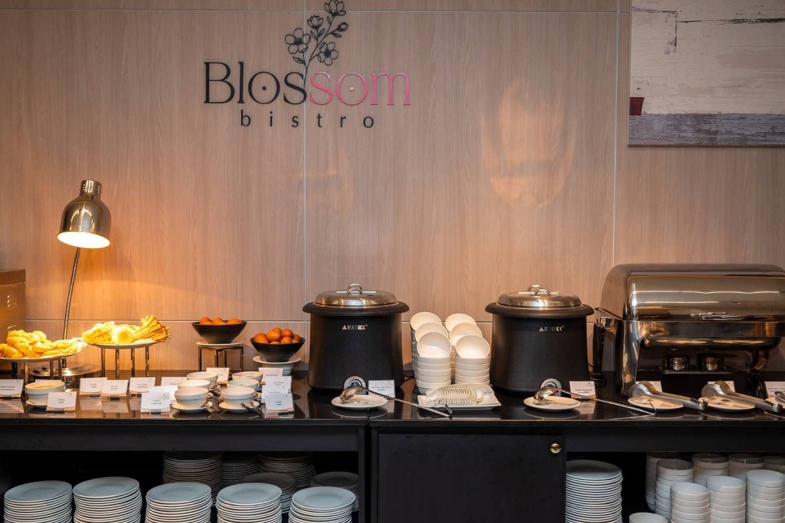 Breakfast buffet at Blossom Bistro with pastries, coffee urns, and stacked plates against a wood wall
