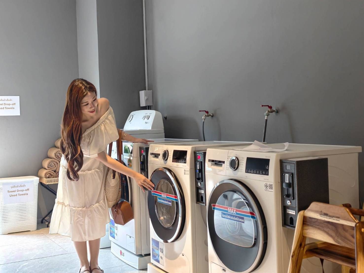 Woman in a light dress using a front-loading washing machine in a laundromat