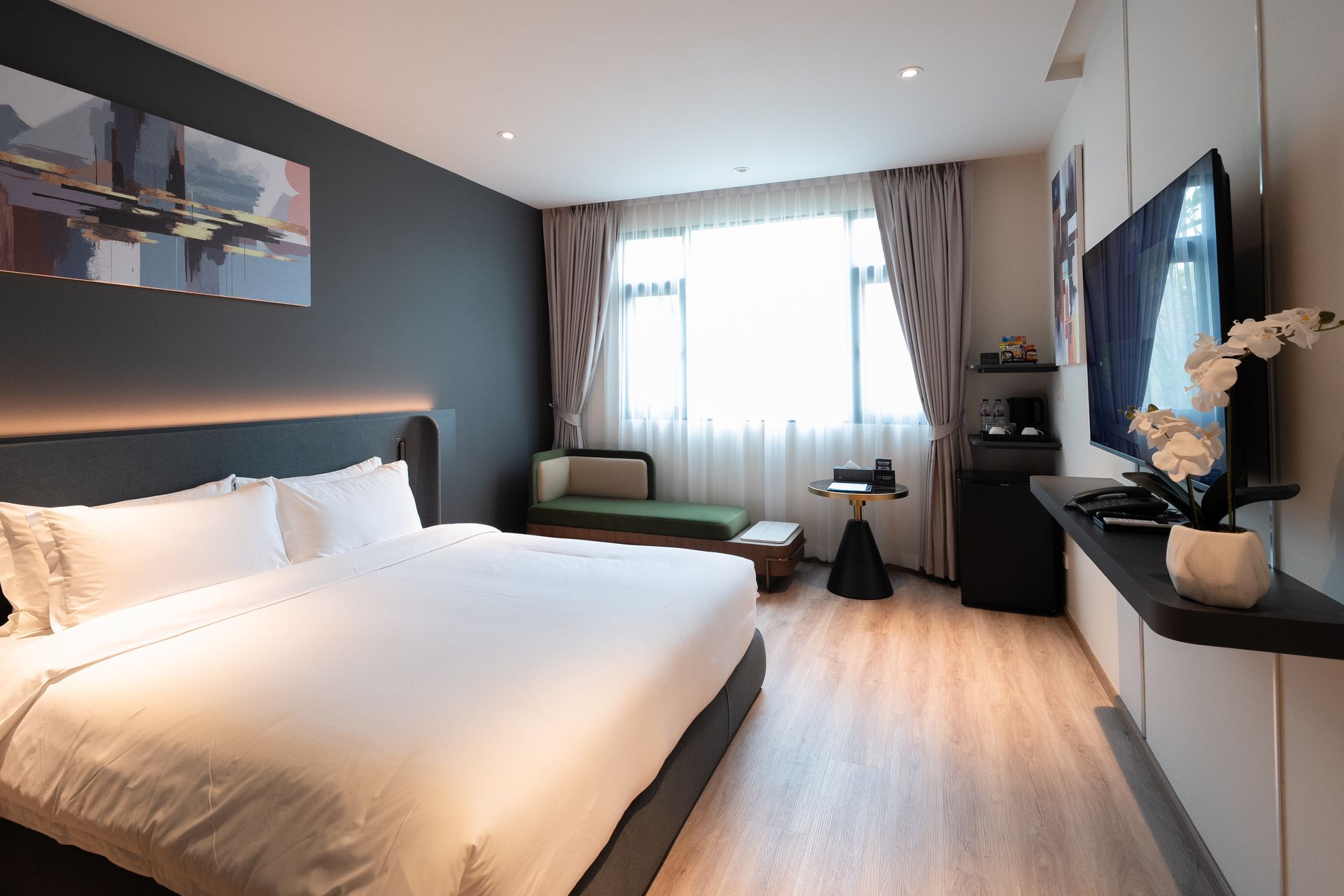 Modern hotel room with a large bed, wall-mounted TV, and bright window curtains
