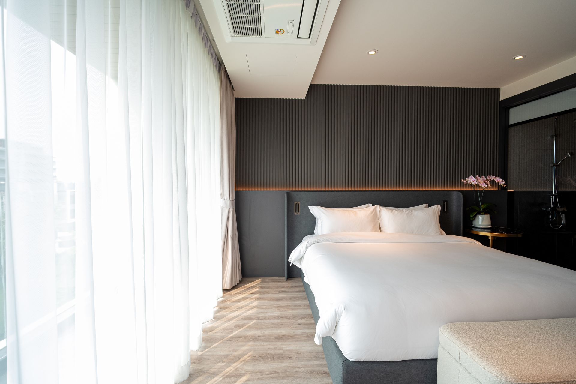 Modern hotel room with white bed, gray walls, and large sheer-curtained windows