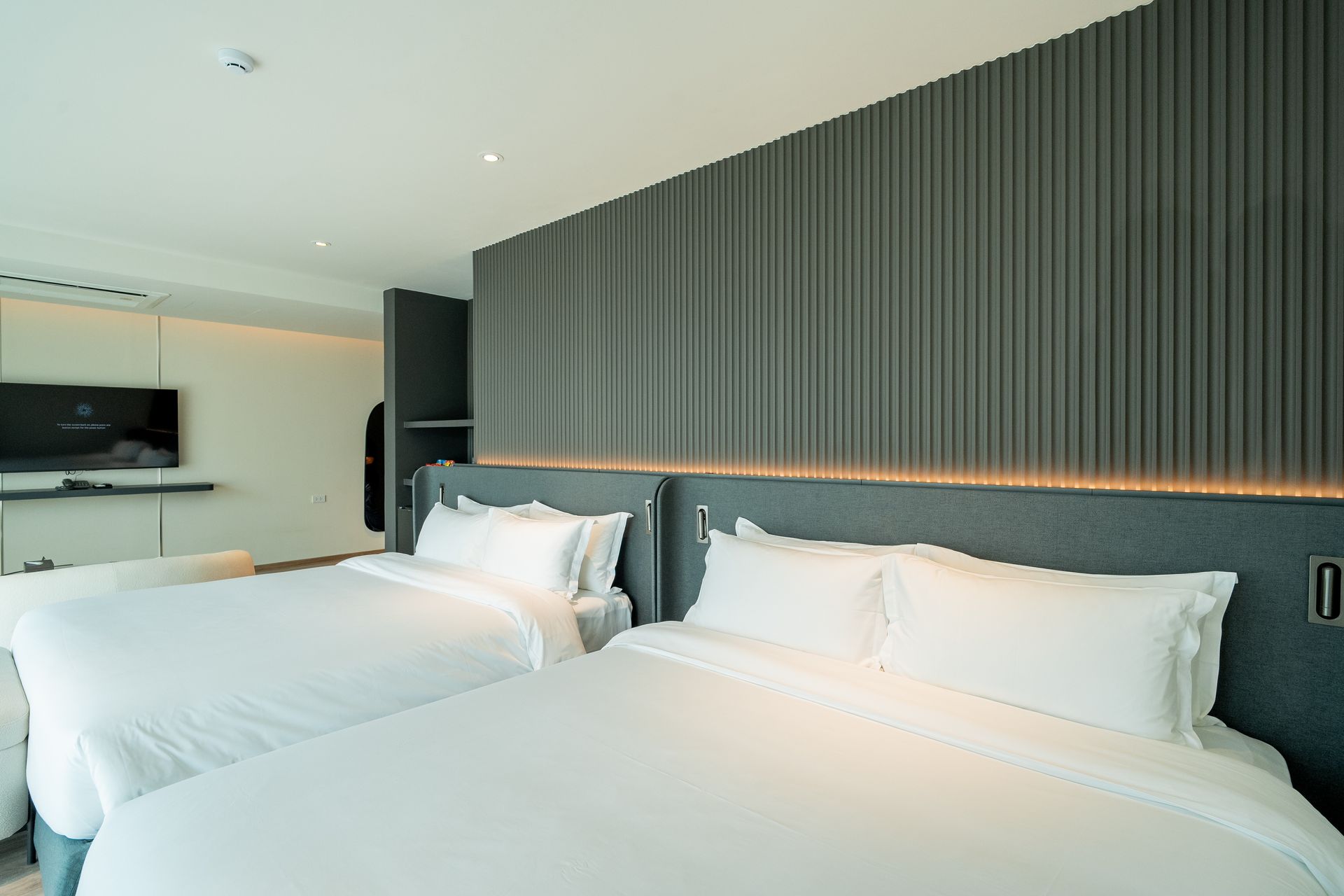 Modern hotel room with two neatly made white beds and a dark wood accent wall
