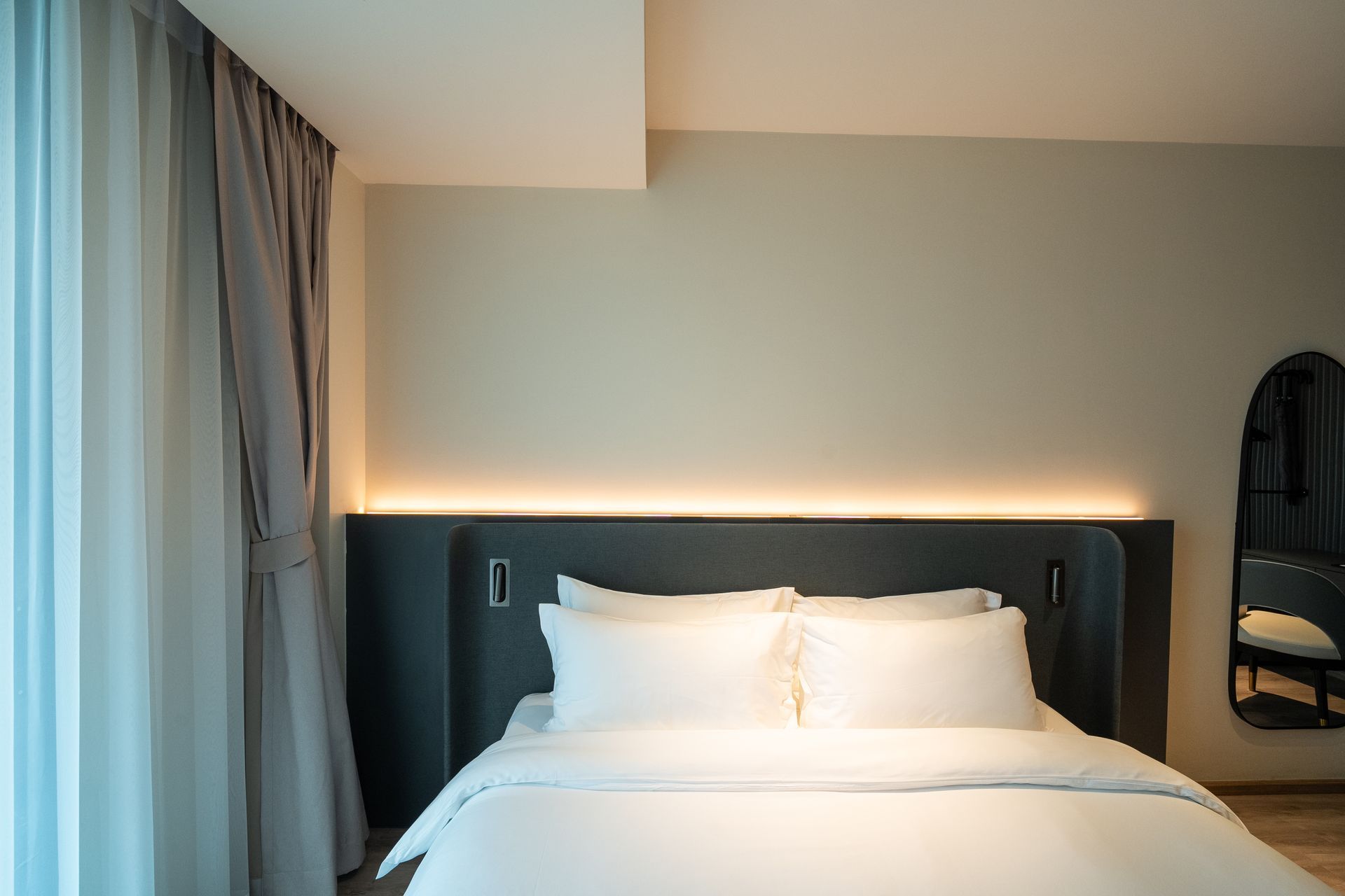 Modern hotel bedroom with a neatly made white bed, dark headboard, and soft wall lighting