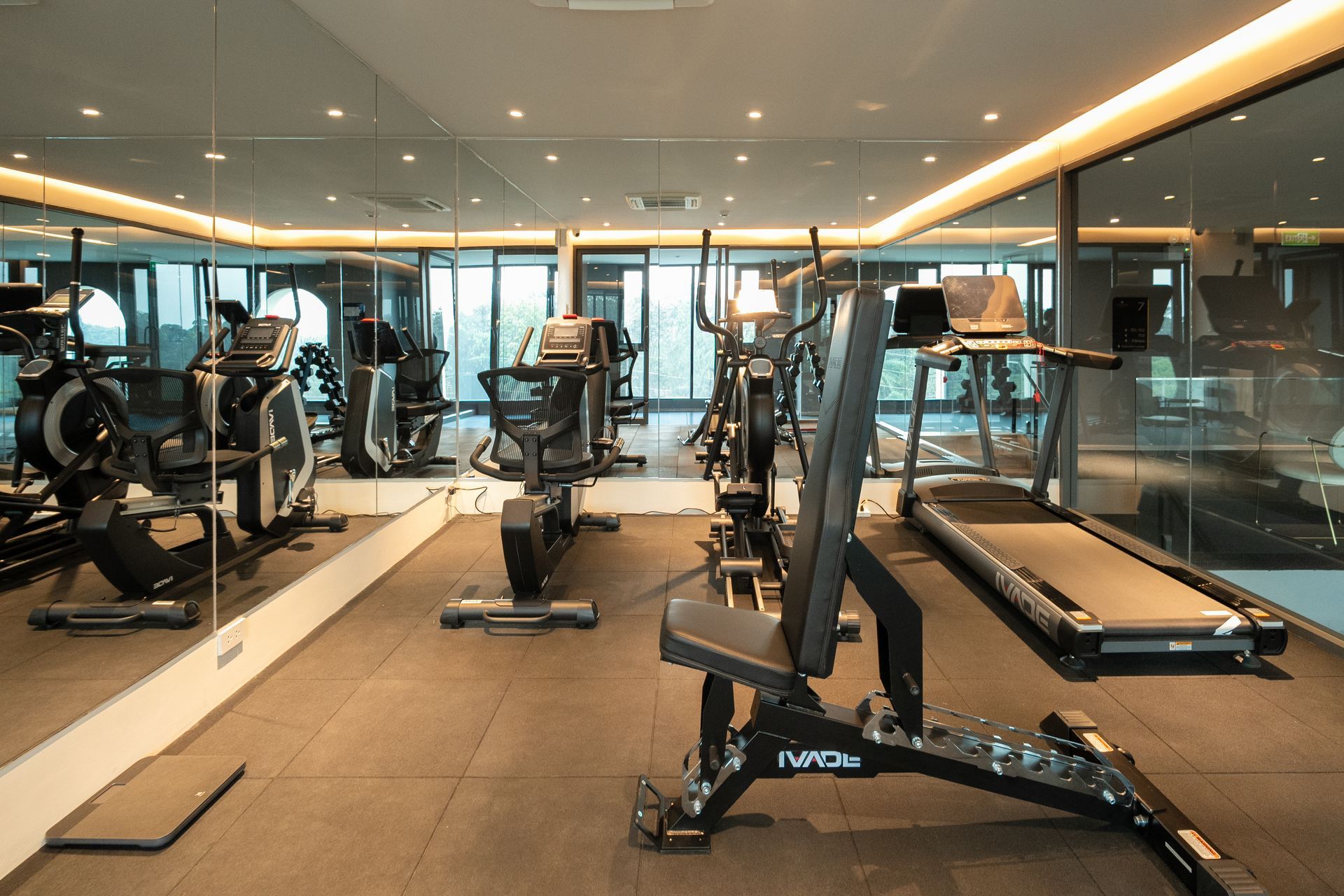 Modern gym with treadmills, stationary bikes, and strength machines in a glass-walled room