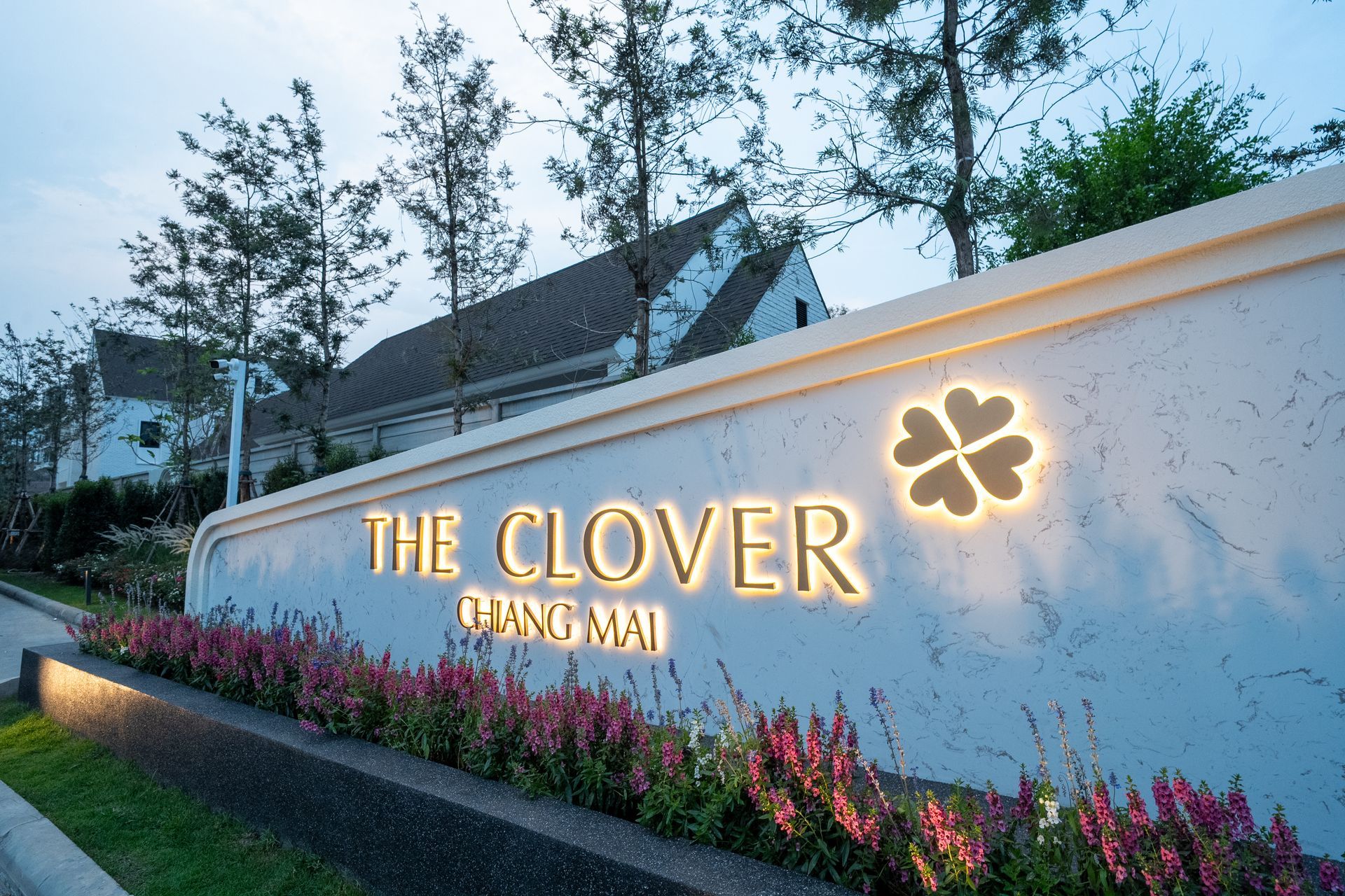 The Clover sign on a white wall with flowers and trees at dusk