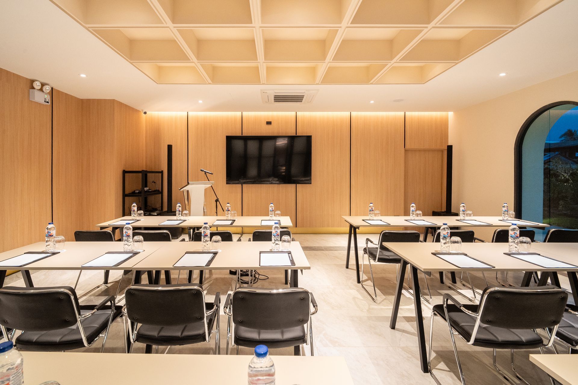 Conference room with long tables, black chairs, wood paneling, and a wall-mounted screen.