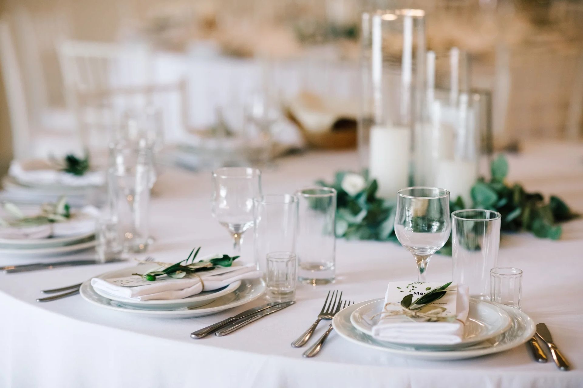 Elegant white table setting with glassware, plates, silverware, and green floral accents at a formal event