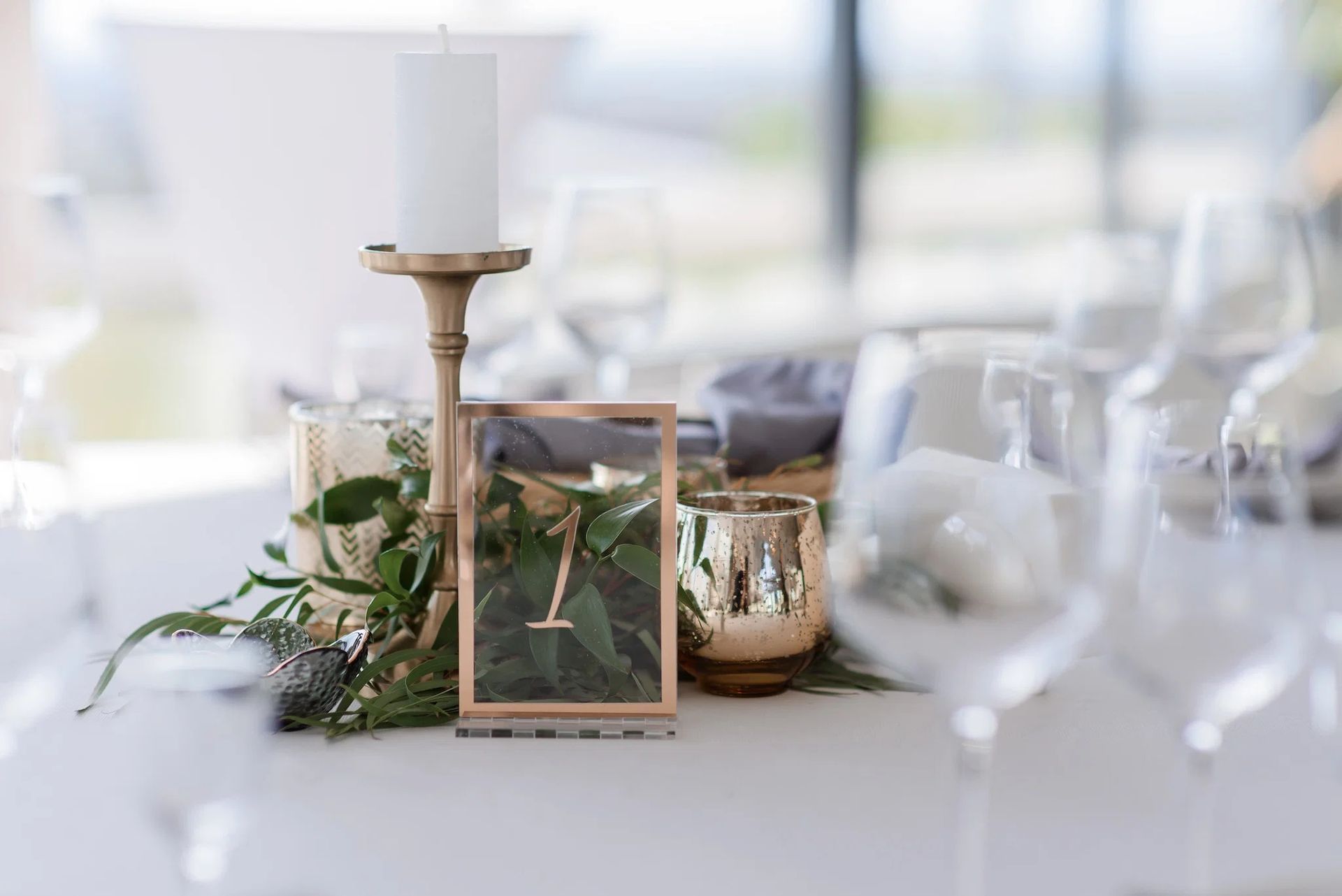 Floral wedding table centerpiece with candle, framed photo, greenery, and gold votive on a white table