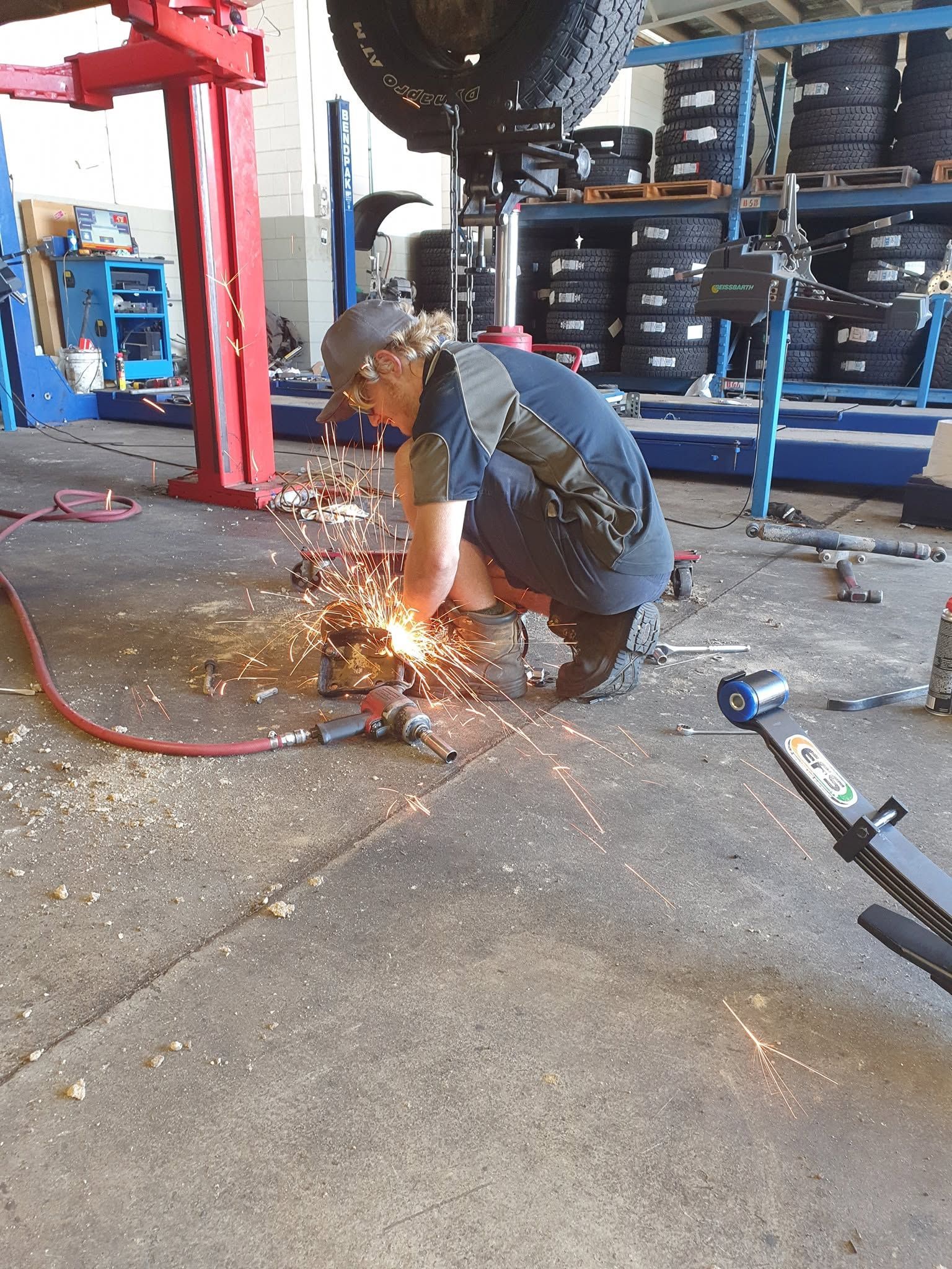 Worker Grinding Metal Under a Red Vehicle Lift, With Bright Sparks in a Garage Workshop — Goodyear Autocare Bowen in Bowen, QLD