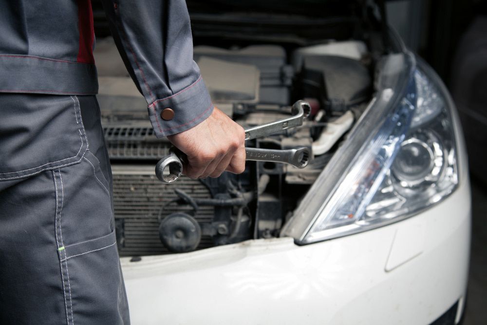 A Mechanic Is Holding A Wrench In Front Of A Car With The Hood Open — Goodyear Autocare Bowen in Bowen, QLD