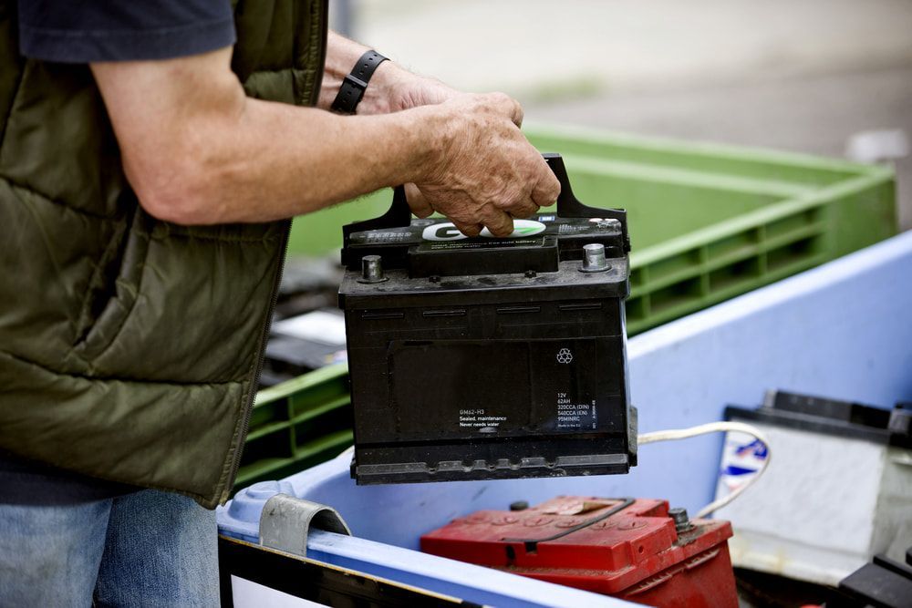 A Man Is Holding A Car Battery In His Hands — Goodyear Autocare Bowen in Bowen, QLD