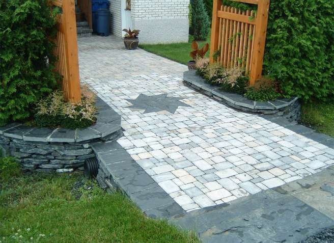 Allée en pierre menant, par un portail de jardin, à une terrasse blanche et à l'entrée de la maison.