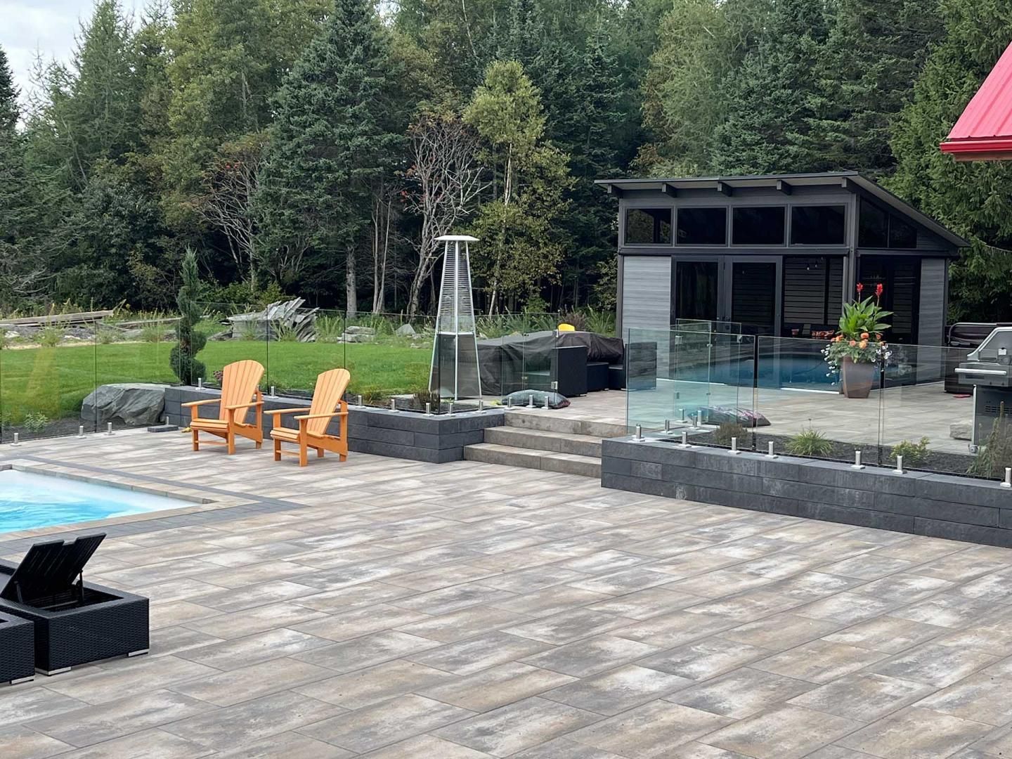 Terrasse avec deux chaises orange, piscine, abri de jardin gris et arbres environnants