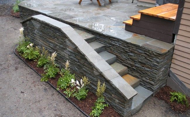 Mur de soutènement en pierre avec marches en béton et petit parterre de fleurs le long d'une allée pavée