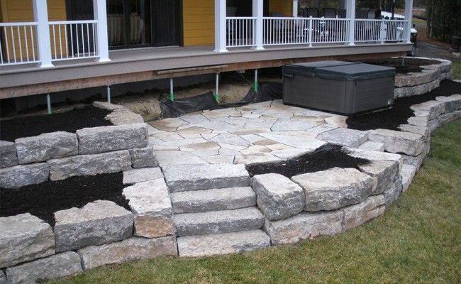 Terrasse en pierre avec muret incurvé et marches menant à une véranda, avec un jacuzzi sur la droite