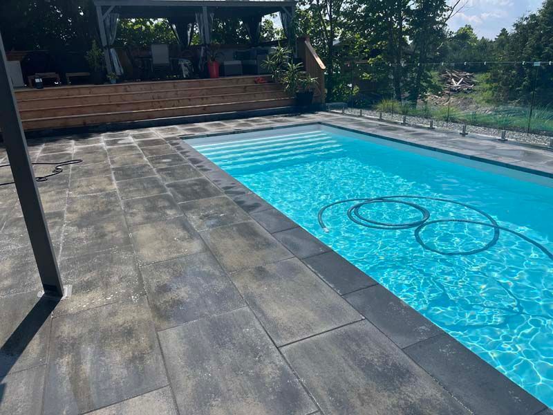 Piscine dans le jardin avec eau bleue, terrasse en pierre et coin salon en bois en arrière-plan