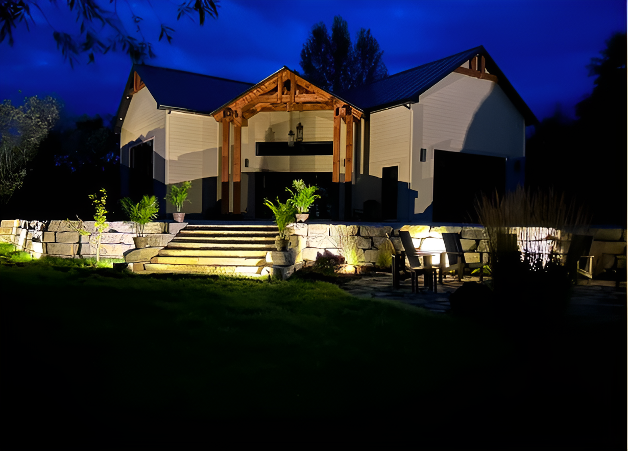 Maison moderne et lumineuse avec marches en pierre et ciel bleu du soir, entourée d'arbres et d'aménagements paysagers.