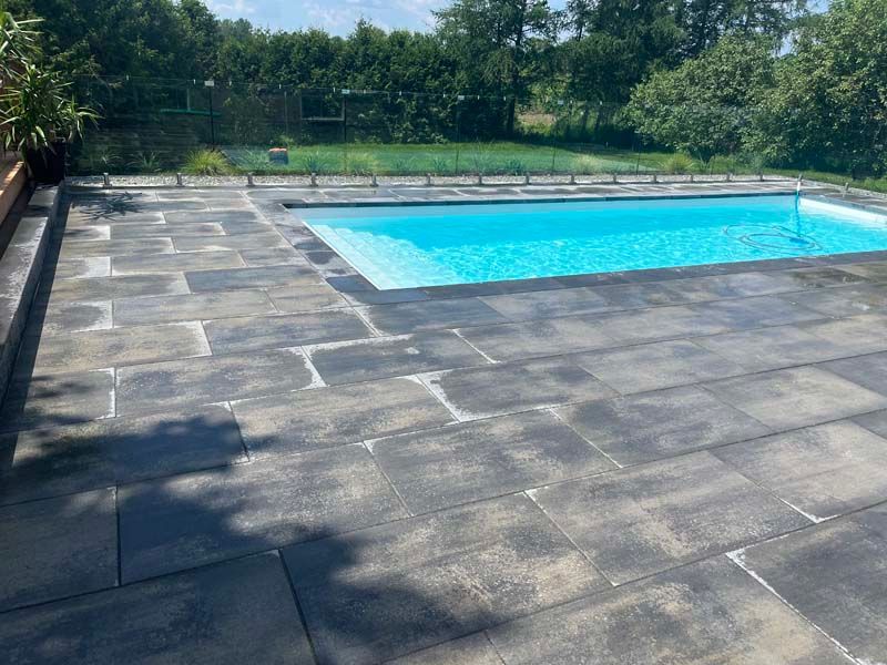 Piscine dans le jardin avec eau bleue et grande terrasse en pierre grise