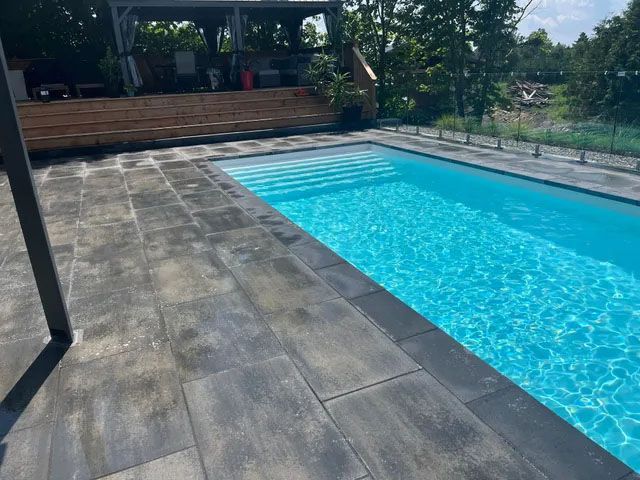 Piscine arrière avec eau bleue et terrasse en pierre baignée de lumière naturelle