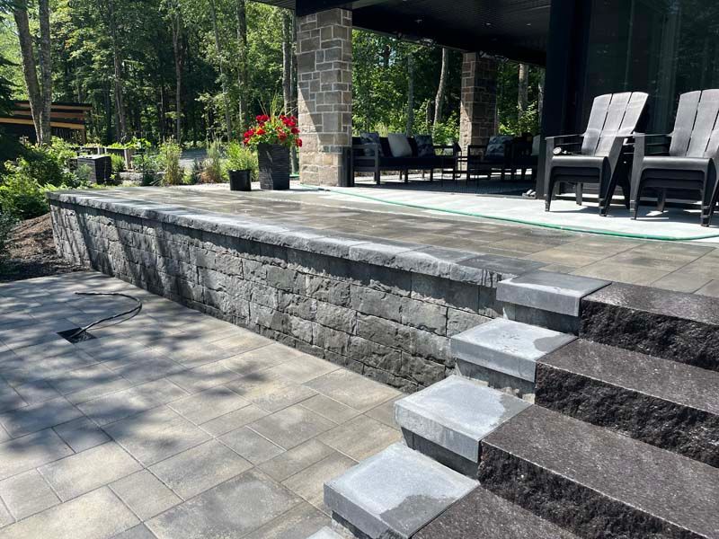 Terrasse en pierre avec marches, muret de soutènement surélevé et coin salon couvert avec chaises et plantes en pot