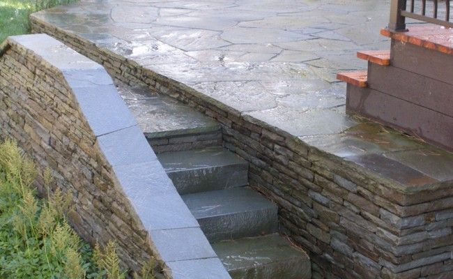 Des marches en pierre longent un muret de briques en pente descendant d'une cour pavée.
