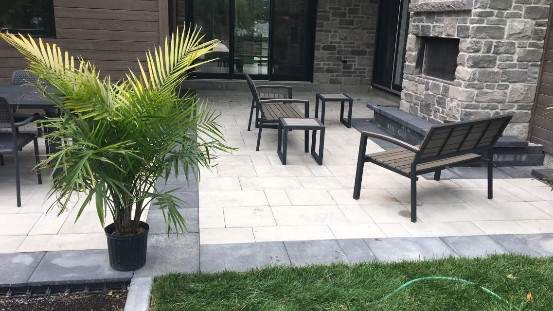 Terrasse avec mobilier de jardin noir, palmier en pot, muret en pierre et bordure de pelouse