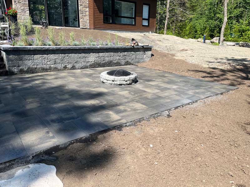 Terrasse en pierre avec foyer circulaire à côté d'une maison et cour en gravier
