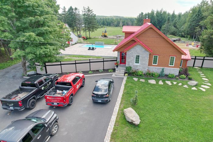 Allée avec trois voitures garées à côté d'une maison en pierre au toit rouge et d'une cour gazonnée, vue d'en haut.