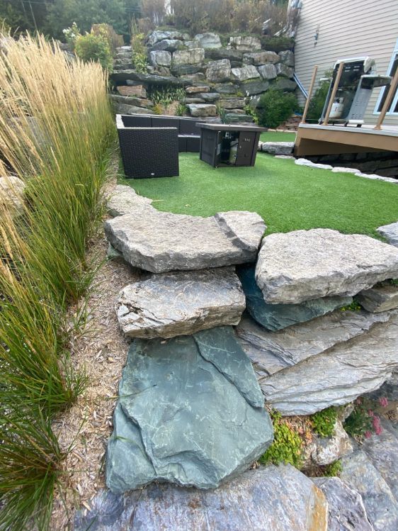 Escaliers en pierre et gazon synthétique dans une cour arrière paysagée avec graminées ornementales et mobilier de jardin